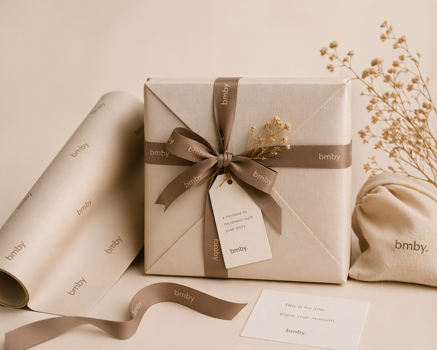 Gift box with ribbon and tag on a beige background, featuring the brand 'bmby'.
